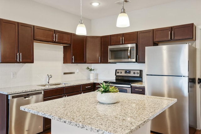 kitchen featuring pendant lighting, sink, decorative backsplash, light stone counters, and stainless steel appliances