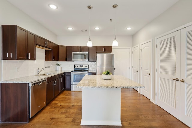 kitchen featuring sink, hanging light fixtures, hardwood / wood-style floors, a kitchen island, and appliances with stainless steel finishes