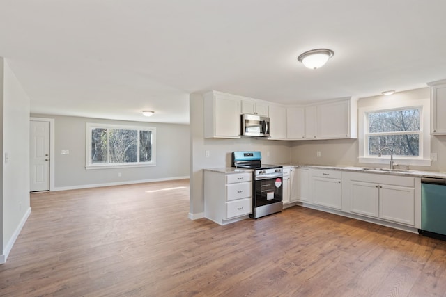 kitchen with appliances with stainless steel finishes, light hardwood / wood-style floors, white cabinetry, and sink