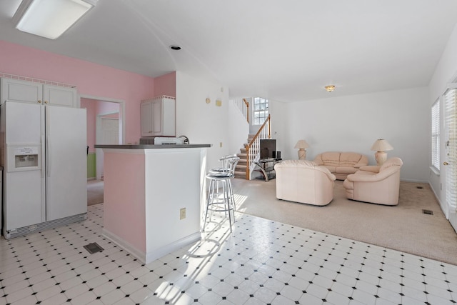 kitchen with light colored carpet, white cabinetry, and white fridge with ice dispenser