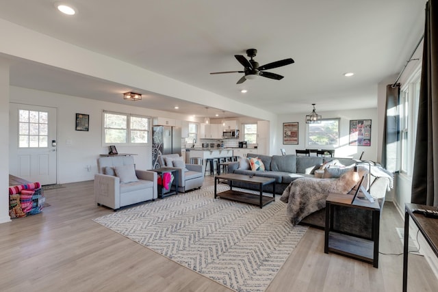 living room featuring ceiling fan with notable chandelier and light wood-type flooring