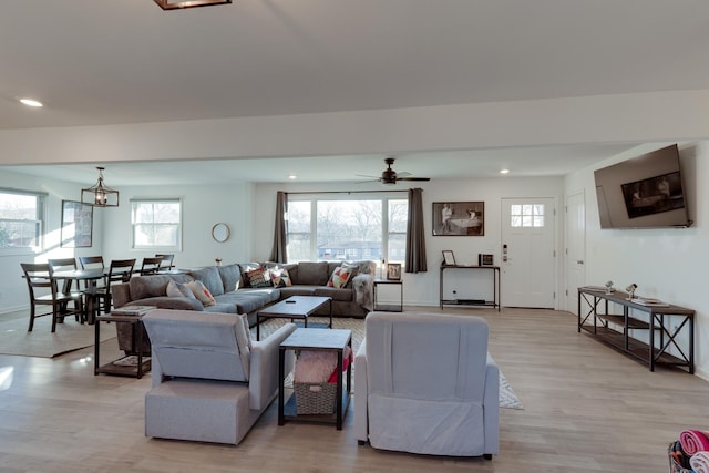 living room with ceiling fan with notable chandelier, light wood-type flooring, and plenty of natural light