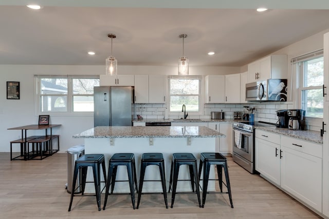 kitchen with sink, hanging light fixtures, stainless steel appliances, a kitchen island, and white cabinets