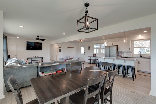 dining space featuring sink, ceiling fan with notable chandelier, and light wood-type flooring