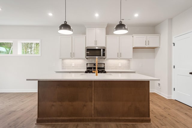 kitchen with a kitchen island with sink, decorative light fixtures, light hardwood / wood-style flooring, white cabinets, and black gas stove