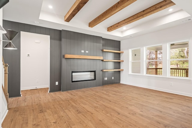 unfurnished living room with beamed ceiling, a large fireplace, light hardwood / wood-style flooring, and wooden walls