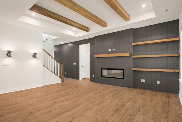 unfurnished living room with beam ceiling, light wood-type flooring, a large fireplace, and wooden walls