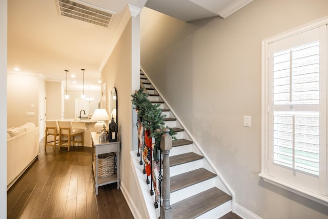 stairs featuring hardwood / wood-style floors, crown molding, and sink