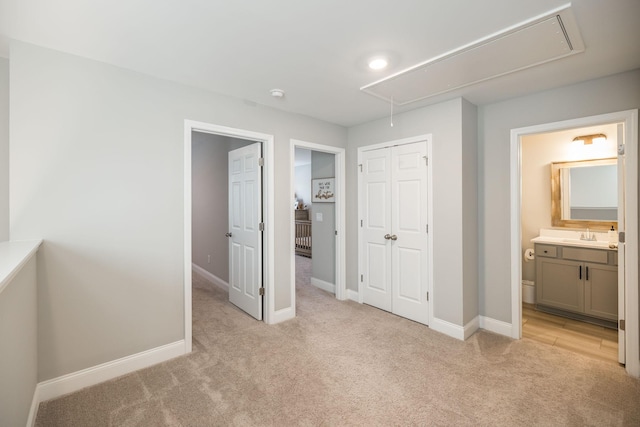 unfurnished bedroom with light colored carpet, ensuite bath, a closet, and sink