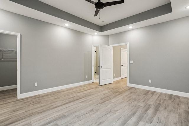 unfurnished bedroom featuring ceiling fan, light hardwood / wood-style floors, a walk in closet, and a closet