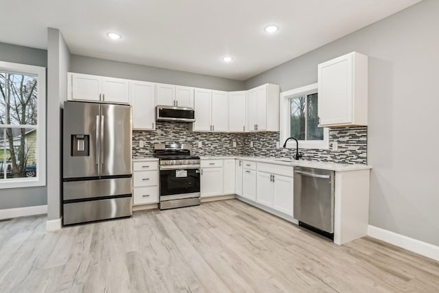 kitchen featuring white cabinets, decorative backsplash, appliances with stainless steel finishes, and light hardwood / wood-style flooring