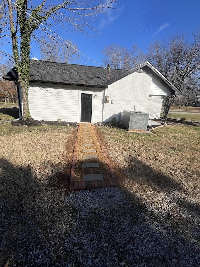 rear view of house with central AC unit and a yard