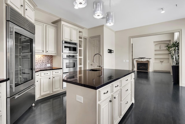 kitchen with appliances with stainless steel finishes, dark hardwood / wood-style flooring, a kitchen island with sink, sink, and decorative light fixtures