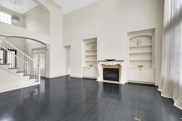 unfurnished living room with built in shelves, dark hardwood / wood-style floors, crown molding, and a high ceiling