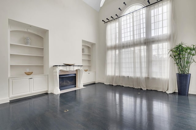 unfurnished living room with built in shelves, dark hardwood / wood-style flooring, and a high ceiling