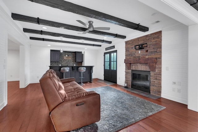 living room featuring dark hardwood / wood-style flooring, ornamental molding, ceiling fan, beam ceiling, and a stone fireplace