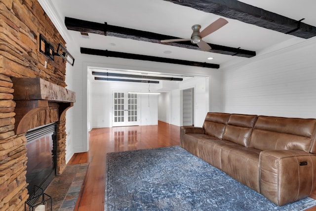 unfurnished living room with beam ceiling, dark hardwood / wood-style floors, a stone fireplace, and ceiling fan