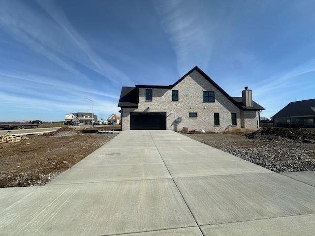 view of side of property with concrete driveway, stone siding, a chimney, and an attached garage