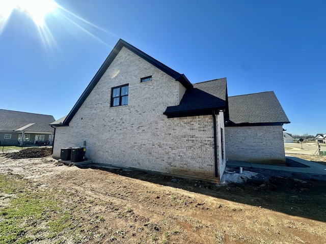 view of home's exterior featuring cooling unit and roof with shingles