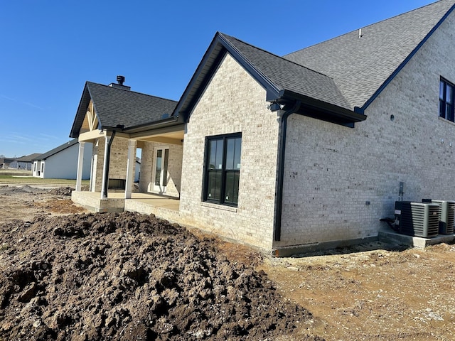 view of side of property with a patio, a shingled roof, central AC, and brick siding