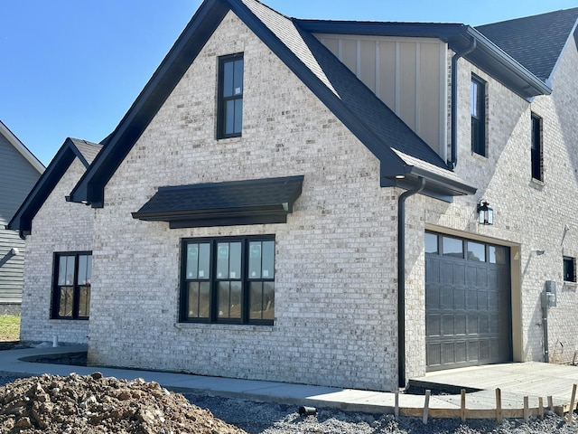 view of side of property featuring driveway, board and batten siding, and brick siding