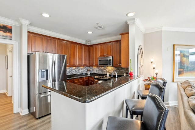 kitchen with stainless steel appliances, kitchen peninsula, crown molding, dark stone countertops, and a breakfast bar