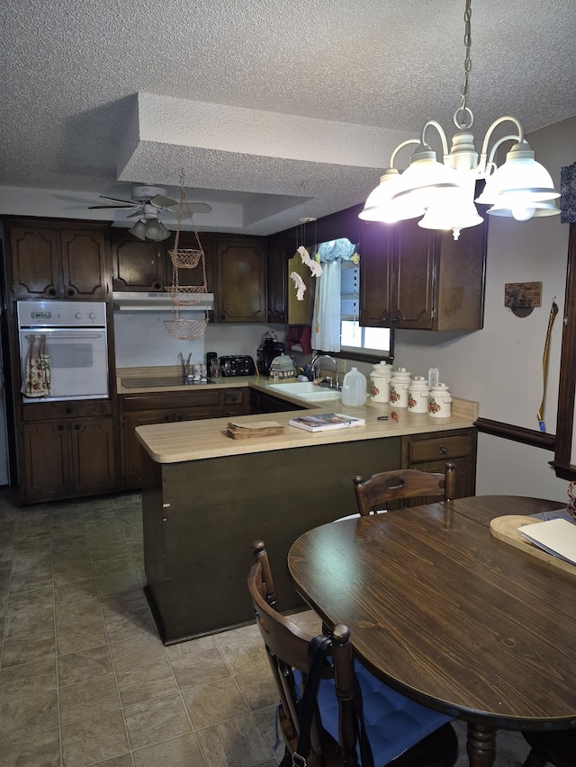 kitchen with dark brown cabinets, a textured ceiling, white oven, sink, and pendant lighting