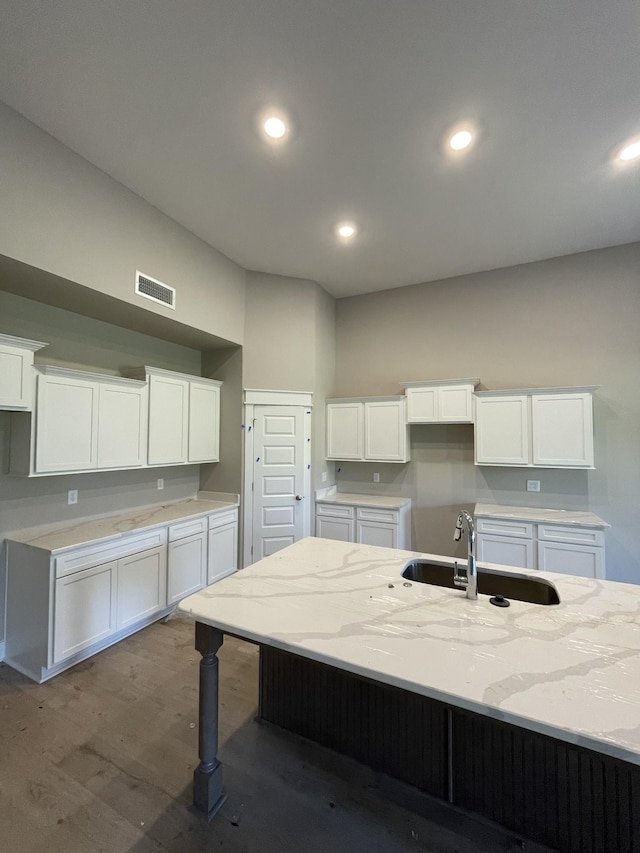 kitchen with sink, white cabinetry, light stone countertops, a center island with sink, and dark hardwood / wood-style flooring