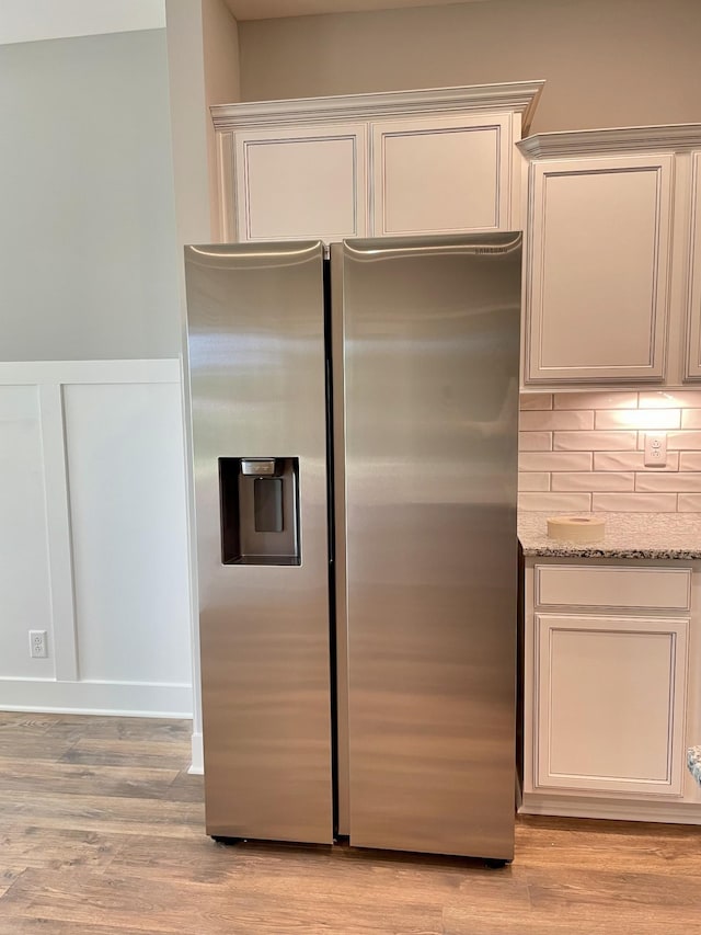 kitchen with light wood-style flooring, light stone counters, stainless steel refrigerator with ice dispenser, and decorative backsplash