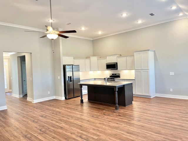 kitchen featuring stainless steel appliances, crown molding, a breakfast bar area, a center island with sink, and light wood-type flooring