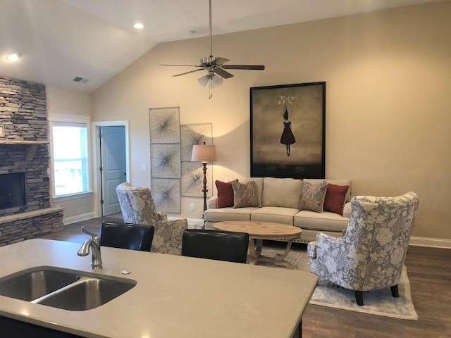 living room featuring dark wood-style floors, lofted ceiling, ceiling fan, a stone fireplace, and baseboards