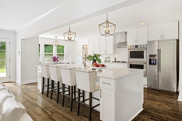 kitchen with a center island with sink, wall chimney exhaust hood, white cabinetry, and stainless steel appliances