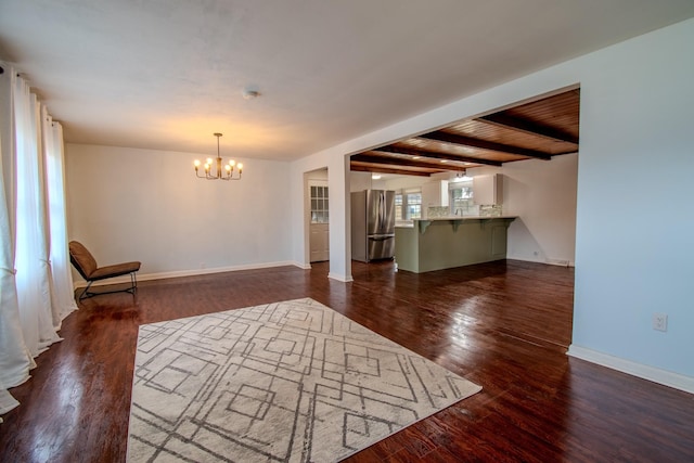 unfurnished living room featuring beamed ceiling, dark hardwood / wood-style flooring, and an inviting chandelier