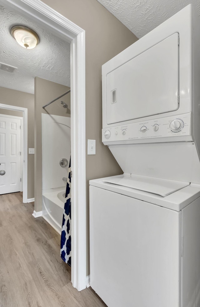 laundry area with a textured ceiling, stacked washer and dryer, and light hardwood / wood-style flooring