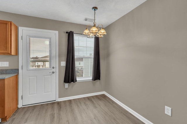 entryway with a notable chandelier, light wood-type flooring, and a textured ceiling