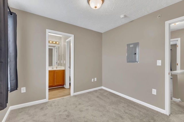 unfurnished bedroom with electric panel, ensuite bathroom, light carpet, and a textured ceiling