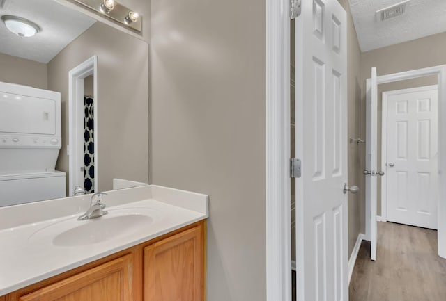 bathroom with a textured ceiling, vanity, wood-type flooring, and stacked washer and dryer