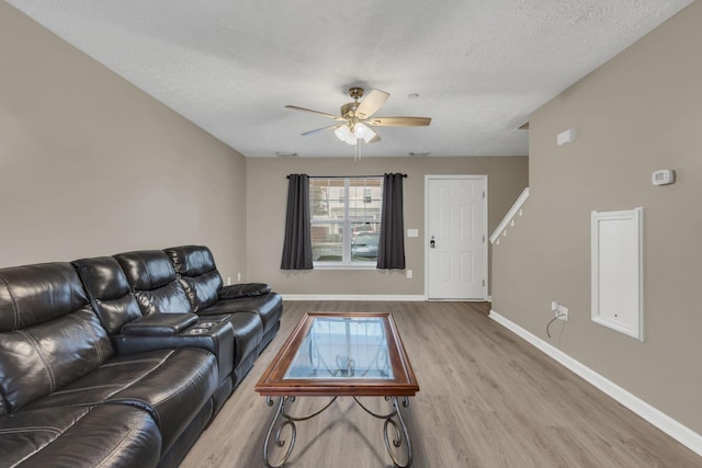 living room with ceiling fan, light wood-type flooring, and a textured ceiling