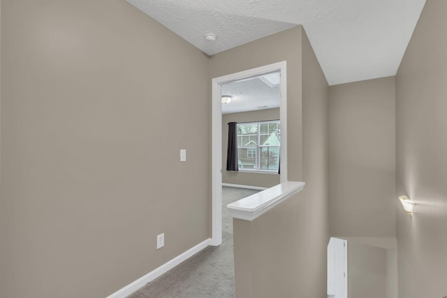 hallway with a textured ceiling and light colored carpet