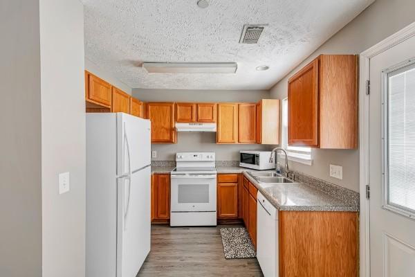 kitchen featuring a textured ceiling, white appliances, sink, and light hardwood / wood-style flooring