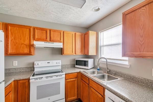 kitchen with a textured ceiling, sink, and white appliances