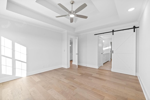 empty room featuring light hardwood / wood-style flooring, ornamental molding, a tray ceiling, ceiling fan, and a barn door