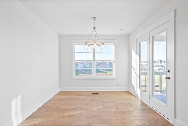 unfurnished dining area with a healthy amount of sunlight, an inviting chandelier, and light hardwood / wood-style flooring