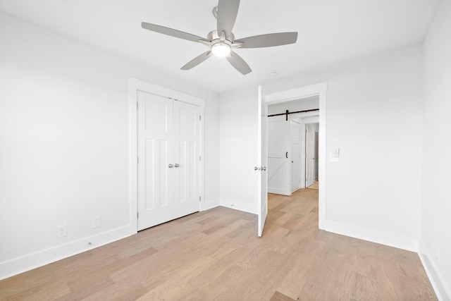 unfurnished bedroom featuring a barn door, light wood-type flooring, ceiling fan, and a closet