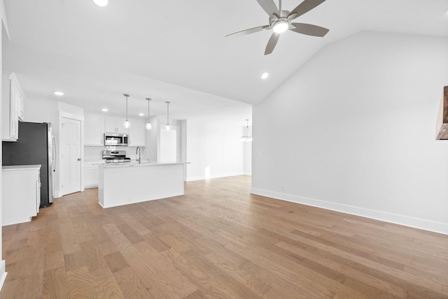 kitchen featuring decorative light fixtures, stainless steel appliances, white cabinets, and a center island with sink