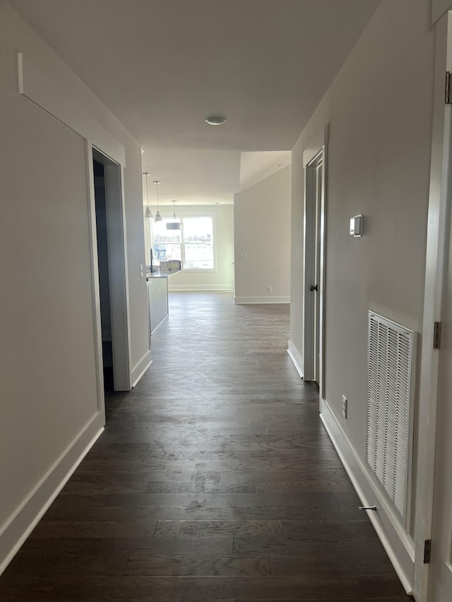 hall with visible vents, baseboards, and dark wood-style flooring