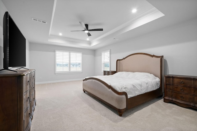 bedroom with ceiling fan, light colored carpet, and a tray ceiling