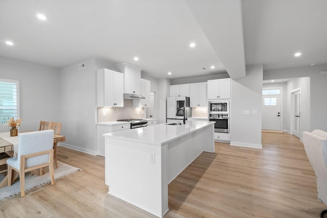 kitchen with white cabinetry, sink, light hardwood / wood-style flooring, a center island with sink, and appliances with stainless steel finishes