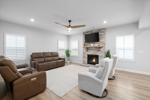 living room with light hardwood / wood-style floors, a stone fireplace, and ceiling fan