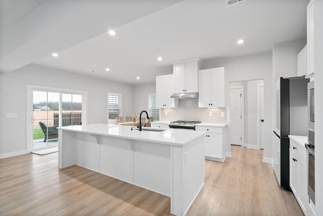 kitchen with stainless steel gas stove, sink, white cabinetry, and an island with sink